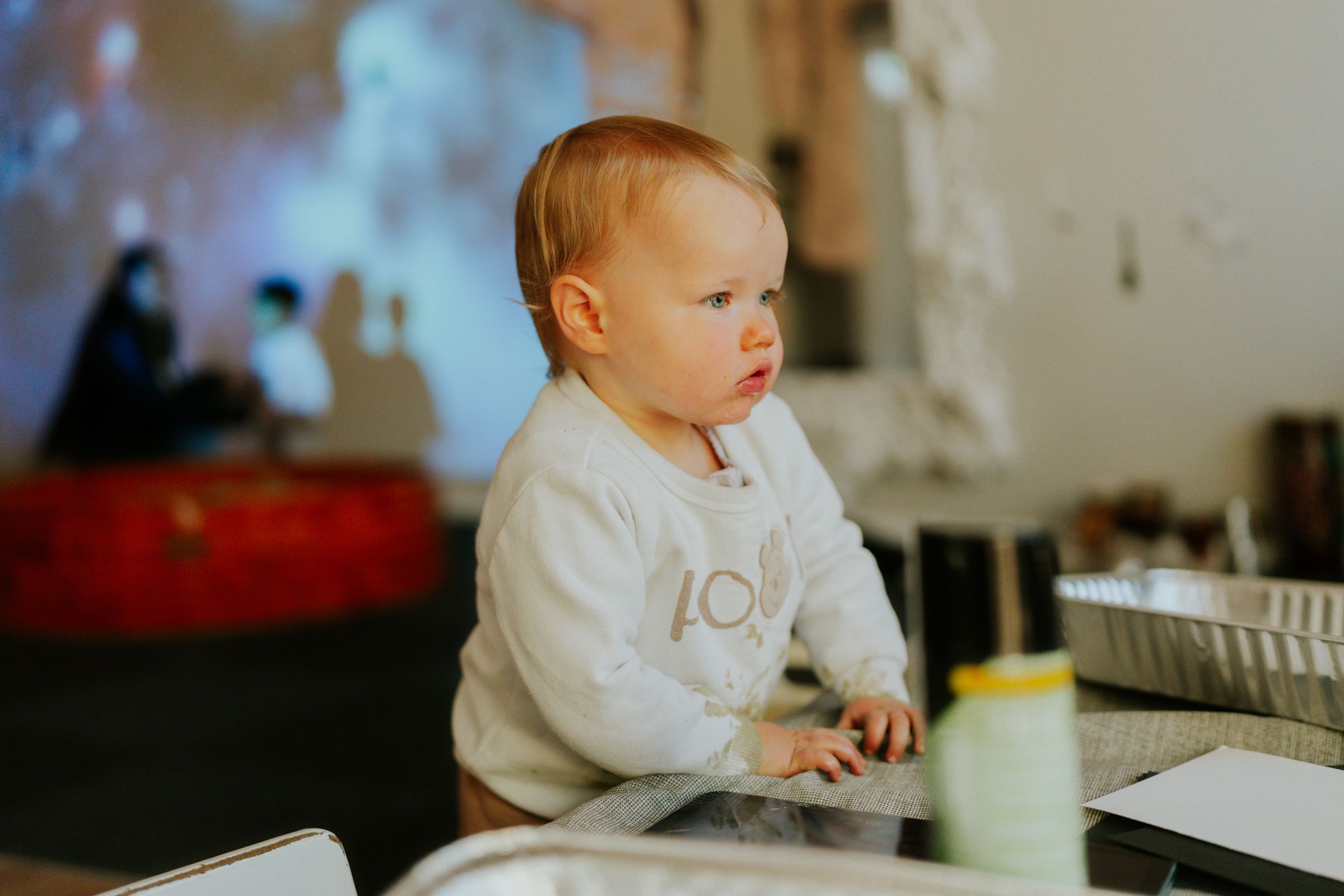 A baby sits at a table, taking in the room