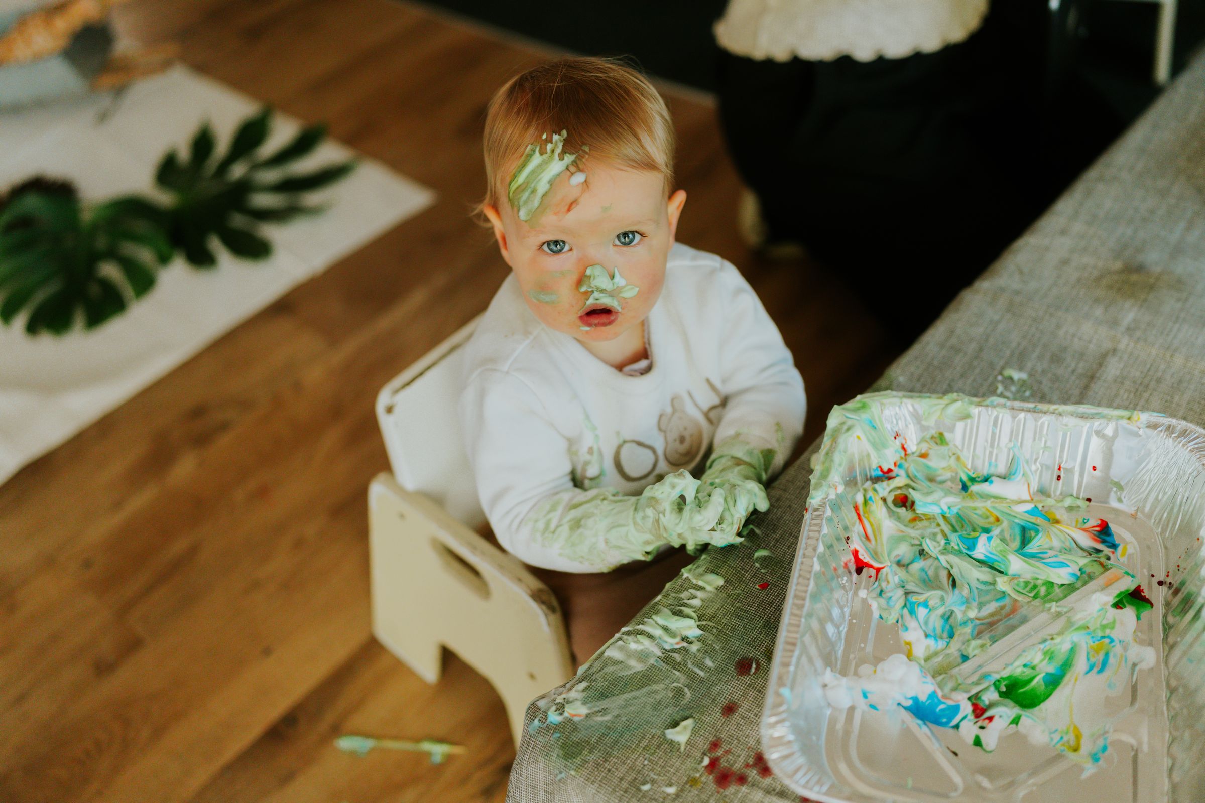 A baby explores paint with hands and face