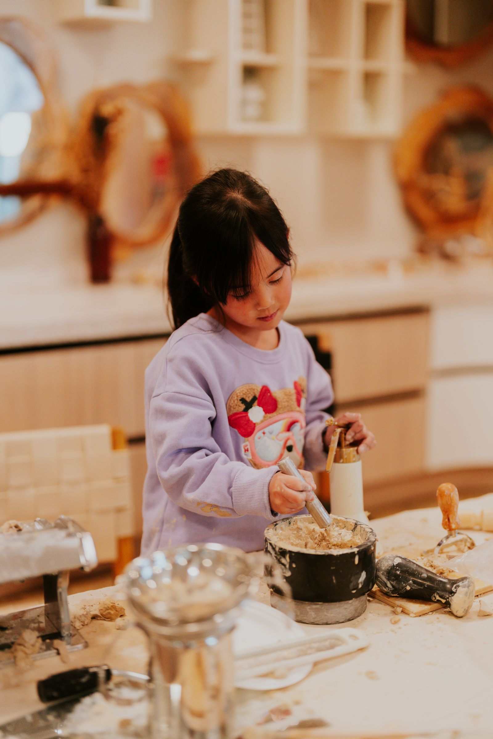 A girl mixes and scoops at the table, absorbed in her work