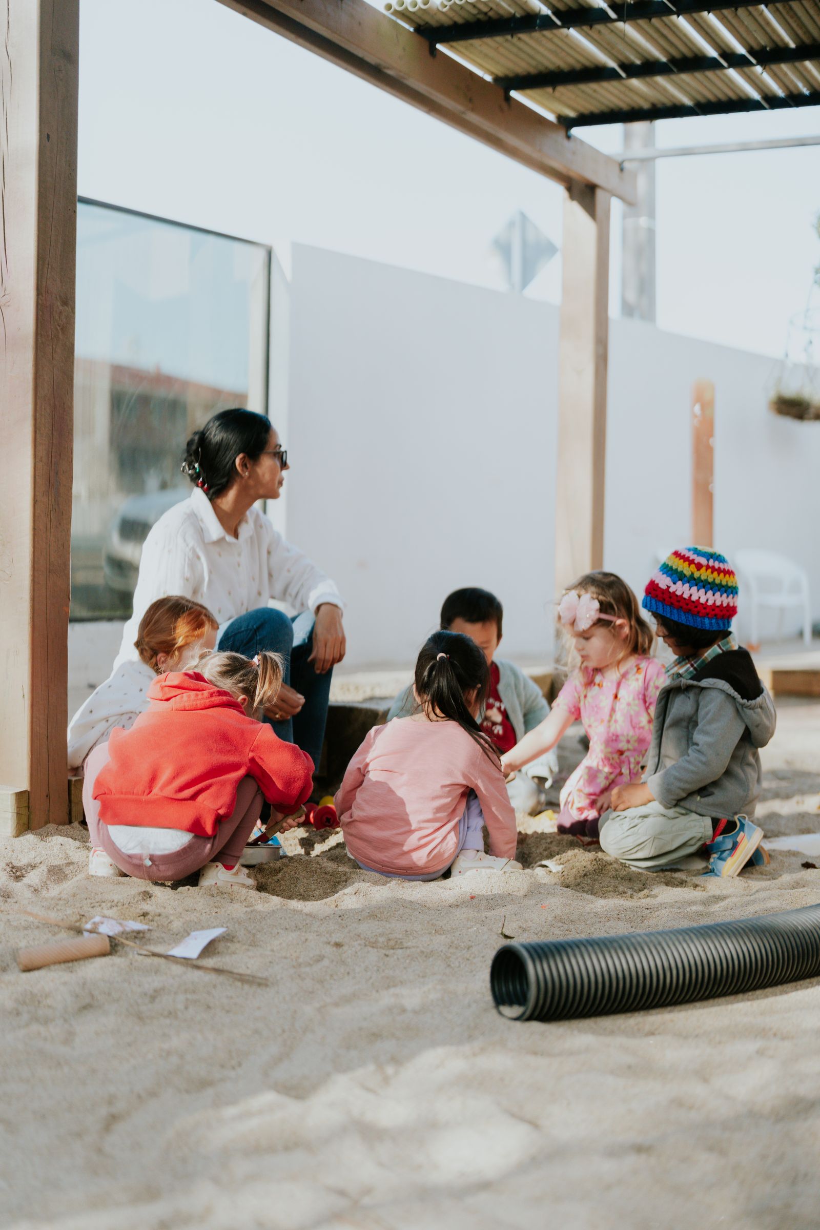 An educator and a group of children play in the sandpit