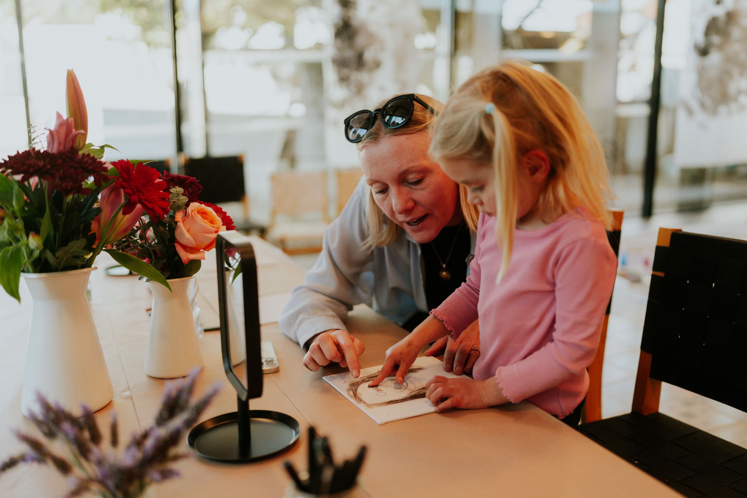 A preschooler draws at the table with an adult beside her