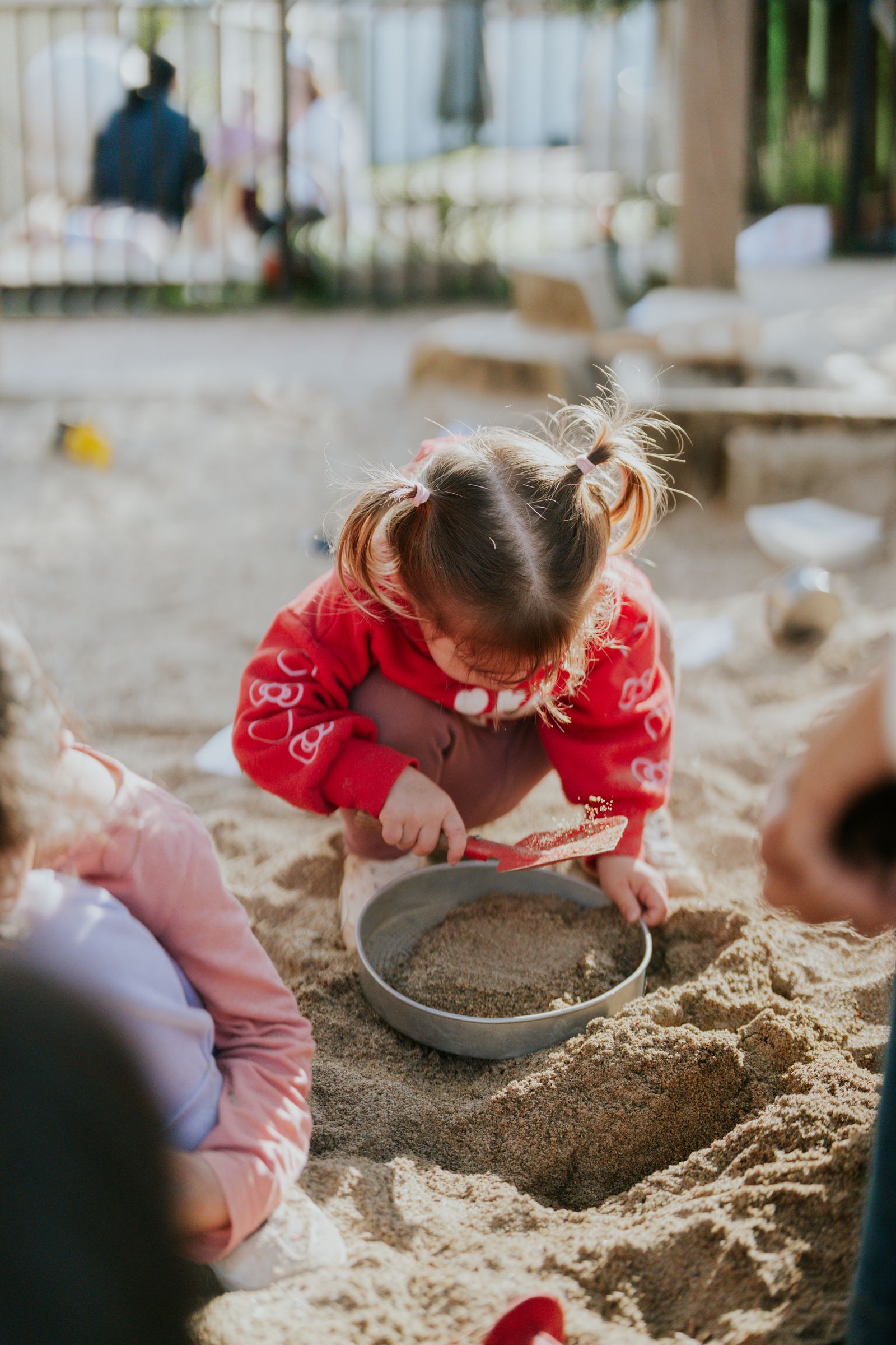 A toddler digs in the sandpit with a bowl