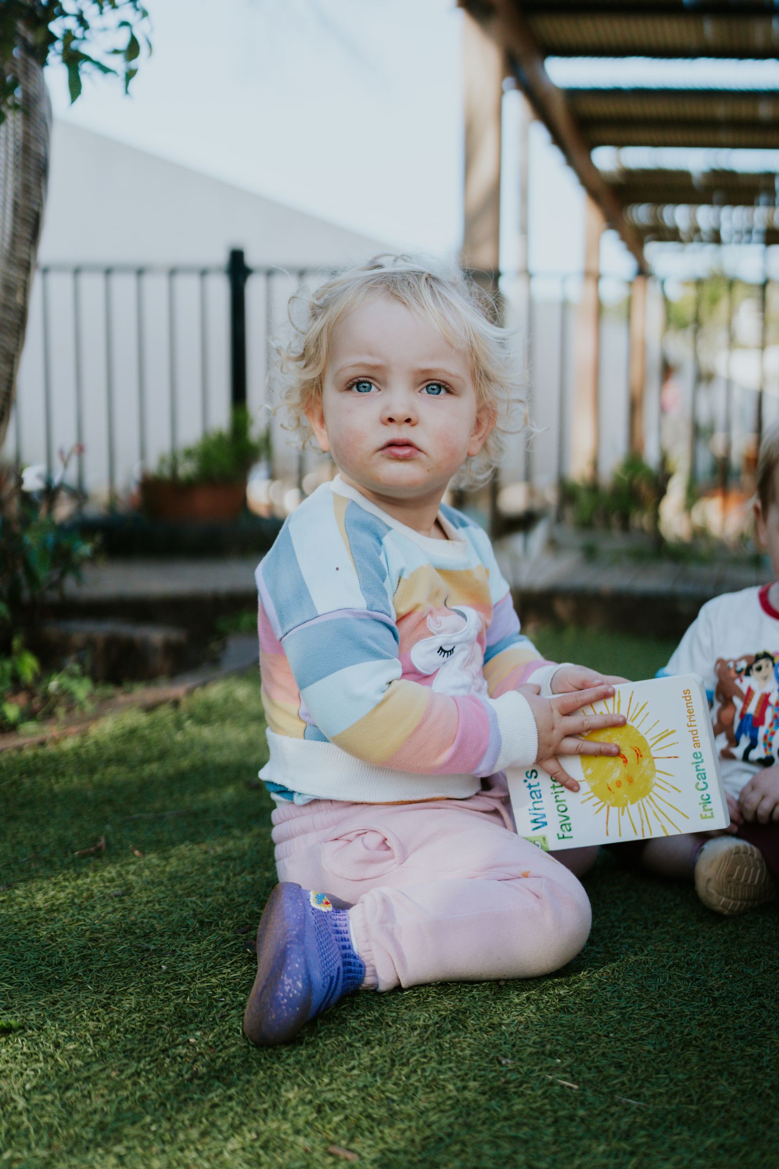 A toddler sits on the grass with a picture book